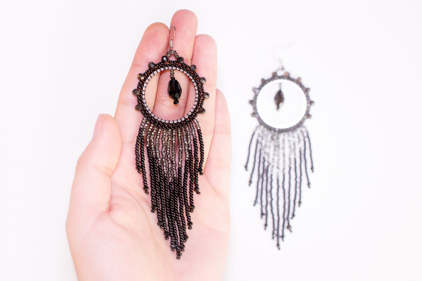 a hand holding a pair of black beaded earrings