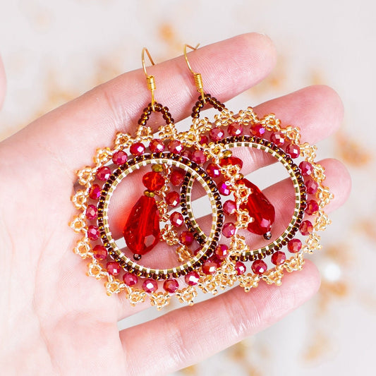 a pair of red and gold earrings on a white surface