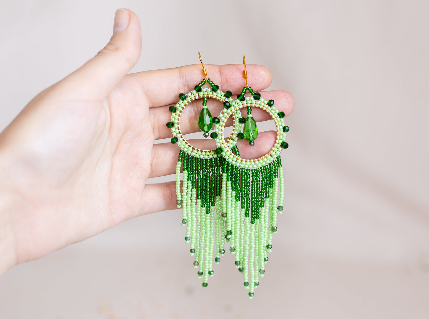 a hand holding a pair of green beaded earrings