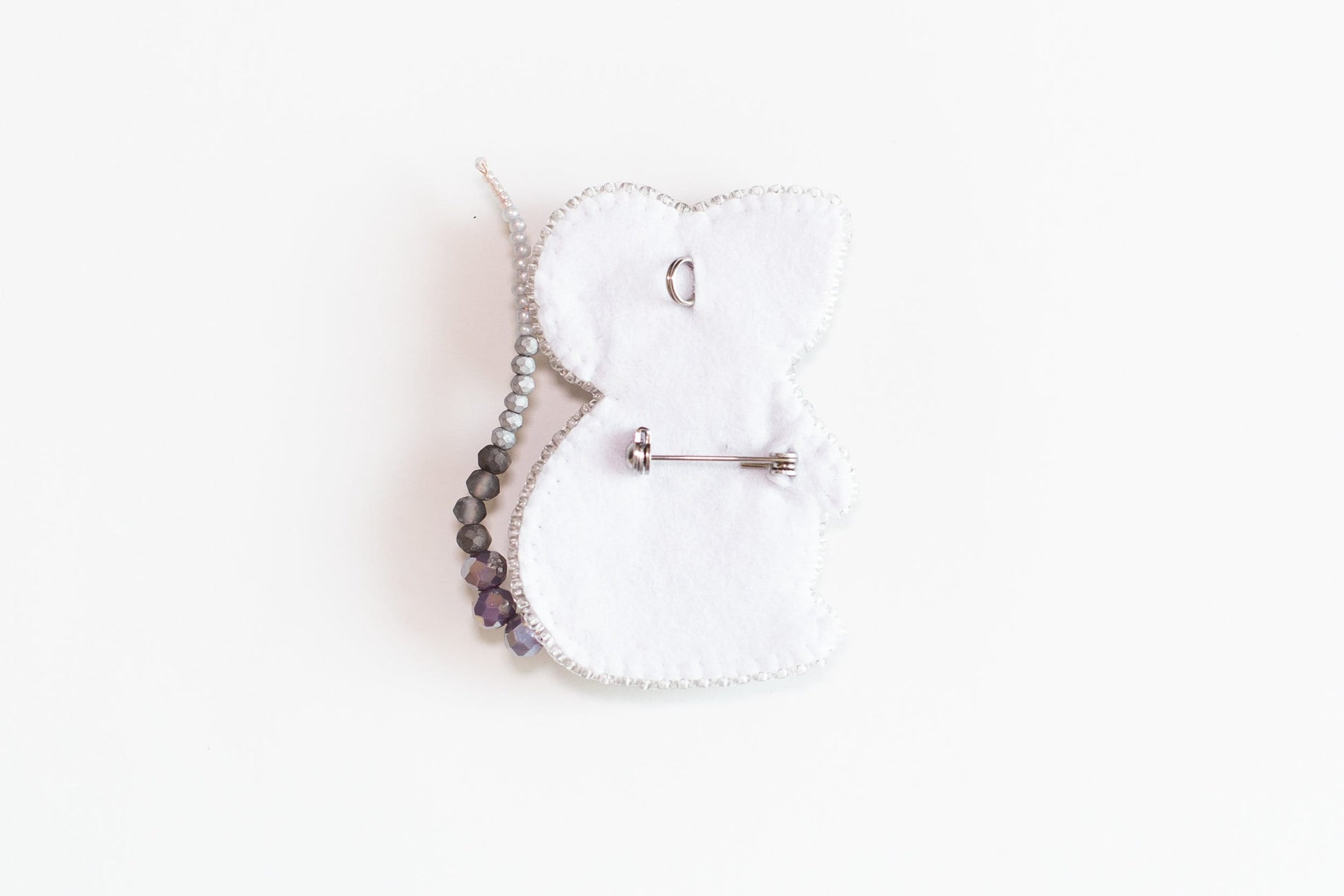 a white teddy bear brooch with a beaded cord