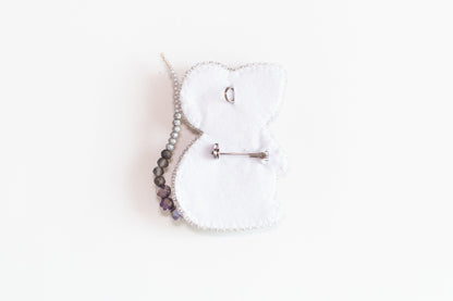 a white teddy bear brooch with a beaded cord