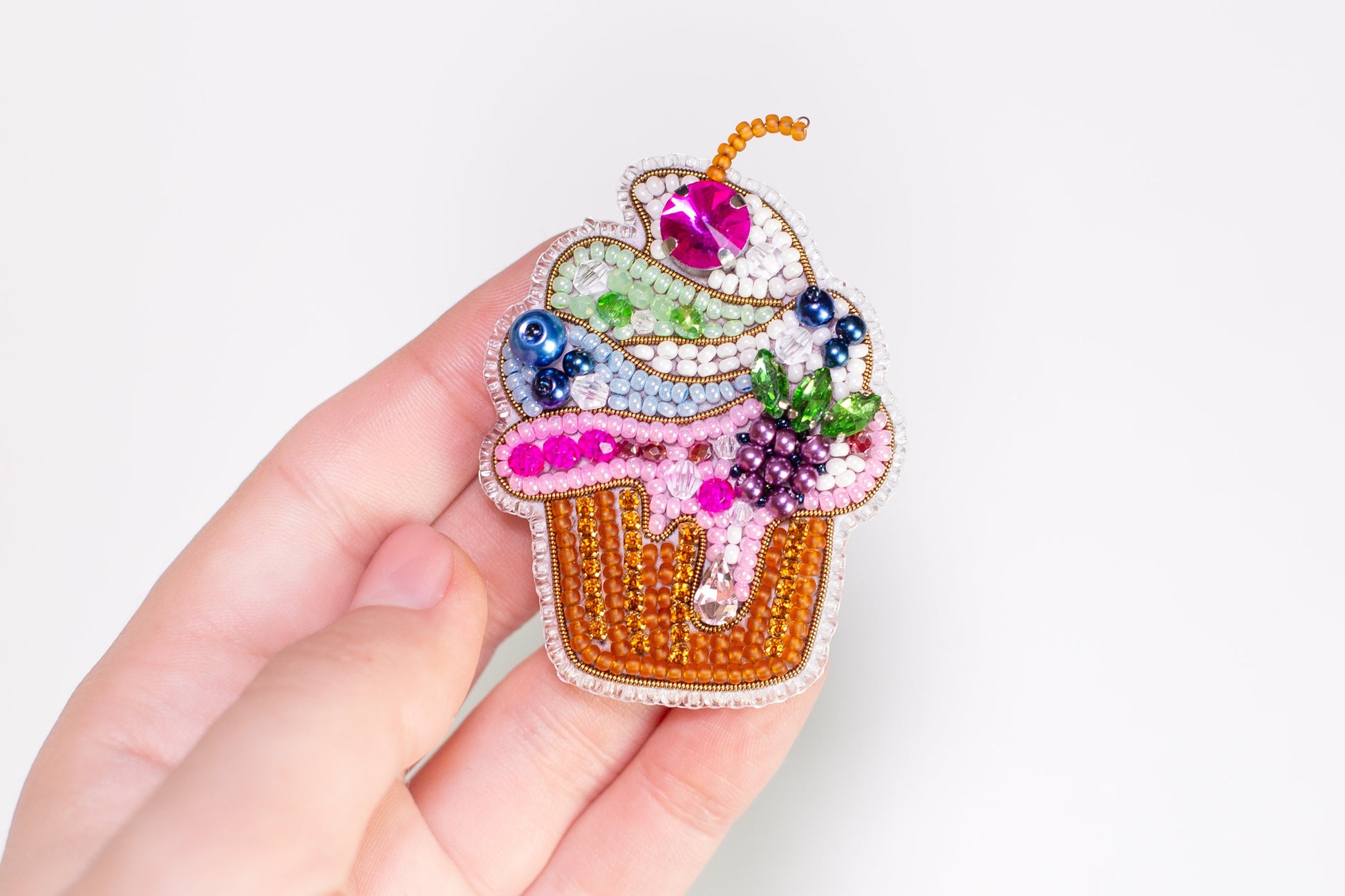 a hand is holding a colorful cupcake brooch