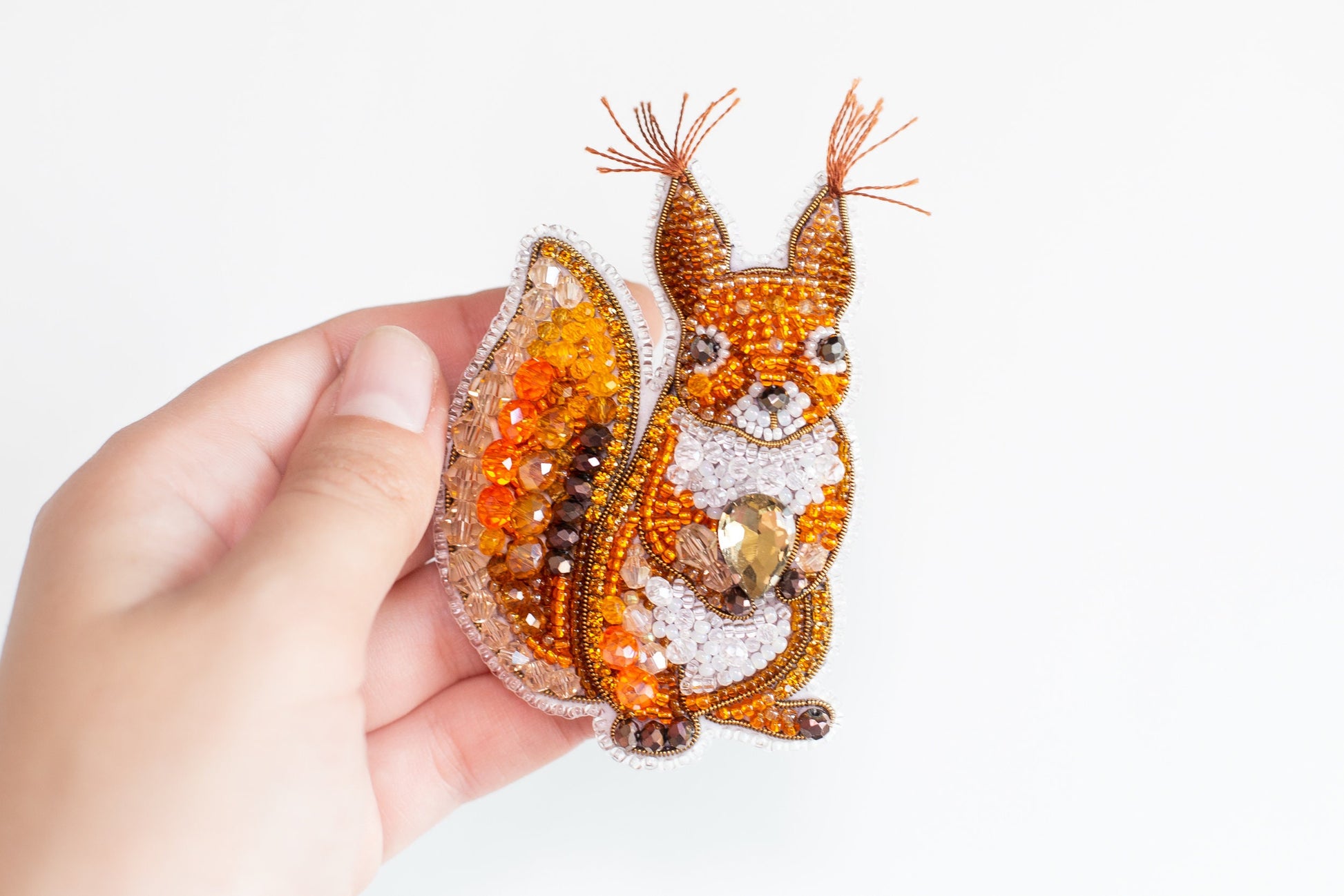 a hand is holding a beaded animal brooch