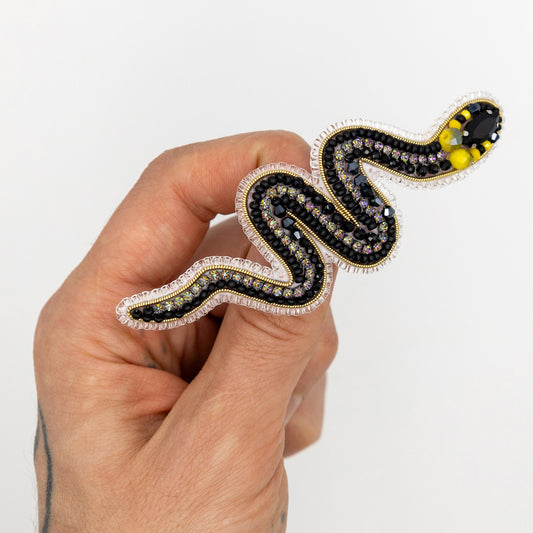 a hand holding a black and yellow snake brooch