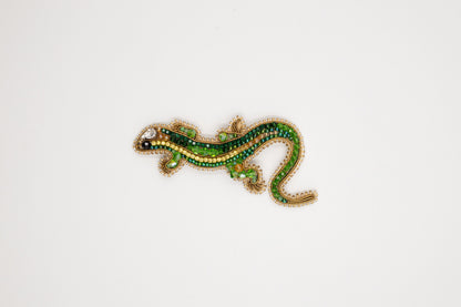 a green and yellow lizard brooch sitting on top of a white surface