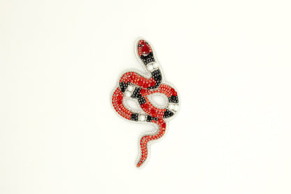 a red, black, and white snake brooch on a white background